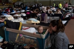 Vlad berusia satu tahun bersama ibunya Natasha terlihat di dalam stadion olahraga dalam ruangan yang digunakan sebagai pusat pengungsi, di desa Medyka, perbatasan antara Polandia dan Ukraina, pada Selasa, 15 Maret 2022. (Foto: AP/Petros Giannakuuri)