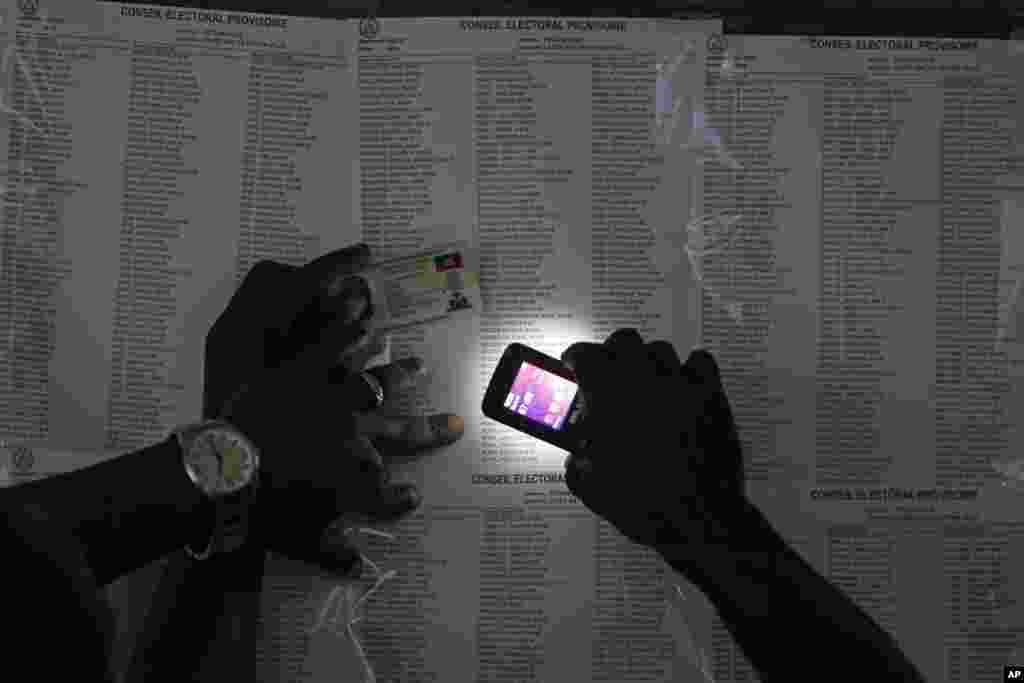 A voter uses his cell phone flashlight to find his name on a voters list during elections in the Petion-Ville suburb of Port-au-Prince, Haiti.