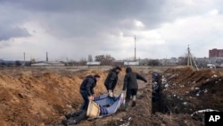 Dead bodies are put into a mass grave on the outskirts of Mariupol, Ukraine, Wednesday, March 9, 2022, as people cannot bury their loved ones because of the heavy shelling by Russian forces. (AP Photo/Evgeniy Maloletka)