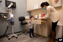 FILE - Hudson Diener, 3, peeks into a cabinet during an appointment for a Moderna COVID-19 vaccine trial in Commack, N.Y., Nov. 30, 2021.
