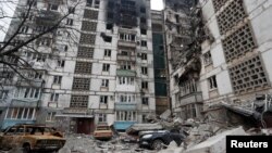 Des voitures détruites sont vues devant un immeuble qui a été fortement endommagé lors du conflit Ukraine-Russie dans la ville portuaire assiégée de Marioupol, le 27 mars 2022.