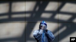A worker in protective suit wipes his face shield at a coronavirus testing side in Beijing, Monday, Dec. 5, 2022. 