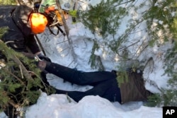 Todd Kautz, a post-doctoral researcher from the State University of New York, lies on his belly to take biological samples from a hibernating bear in its den as a colleague holds his feet in Grand Portage, Minn. on March 2, 2022.