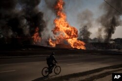 A man rides his bike past flames and smoke rising from a fire following a Russian attack in Kharkiv, Ukraine. (AP Photo/Felipe Dana)