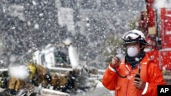 A rescue worker uses a two-way radio transceiver during heavy snowfall at a factory area devastated by an earthquake and tsunami in Sendai, northern Japan, March 16, 2011