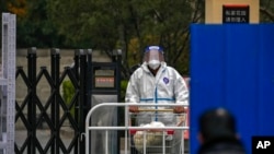 A worker in protective clothing transfers foods to a barricaded neighborhood locked down for health monitoring following a COVID-19 case detected in the area in Beijing, Nov. 9, 2022. 