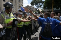FILE - Supporters of Venezuela's opposition face riot police officers who are blocking a street, as they take part in a rally to demand a referendum to remove Venezuela's President Nicolas Maduro, in Caracas, Venezuela, Sept. 16, 2016.