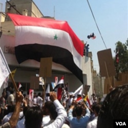 Pendukung Presiden Bashar al-Assad mengibarkan bendera Suriah di halaman Gedung Kedubes AS di Damaskus (11/7).