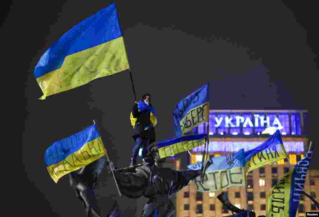 Seorang demonstran pro-integrasi Eropa melambaikan bendera Ukraina sambil berdiri di atas patung selama protes di Lapangan Kemerdekaan di Kiev, 15 Desember 2013.