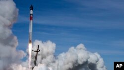 In this image made from video supplied by Rocket Lab, a helicopter hovers above as it attempts to capture Electron's first stage in mid-air by helicopter above New Zealand, Tuesday, May 3, 2022. (Rocket Lab via AP)