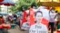 FILE: Protesters walk through a market with posters of ousted Myanmar leader Aung San Suu Kyi in Yangon, Myanmar Thursday, April 8, 2021. She went on trial Monday, May 2, 2022, in a new corruption case against her, alleging she took $550,000 in bribes from a construction magnate.