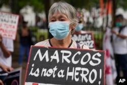 FILE - An activist holds a slogan during a rally outside the Commission on Elections in Manila, Philippines, Nov. 26, 2021.