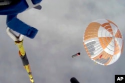 In this image made from video supplied by Rocket Lab, a helicopter hovers above as it attempts to capture Electron's first stage in mid-air by helicopter above New Zealand, Tuesday, May 3, 2022. (Rocket Lab via AP)