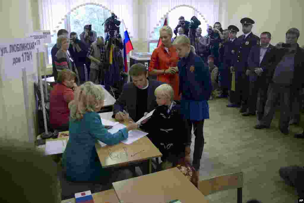 Russian opposition leader Alexei Navalny receives his ballot while his wife Yulia, daughter Daria, and son Zakhar watch at a polling station in Moscow's mayoral election, Sept. 8, 2013. 