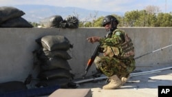 Seorang anggota kepolisian Kenya, yang tergabung dalam pasukan internasional yang didukung PBB untuk Haiti, berlindung di balik tembok dalam baku tembak dengan geng kriminal di Port-au-Prince, Haiti, pada 5 Desember 2024. (Foto: AP/Odelyn Joseph)