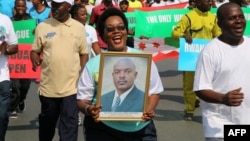 FILE - A woman holds up a picture of Burundi's President Pierre Nkurunziza during a rally in Bujumbura on May 14, 2016, commemorating the one-year anniversary of the failed attempt of a government coup. Authorities in Burundi arrested 11 students last week for defacing a photo of President Pierre Nkurunziza.