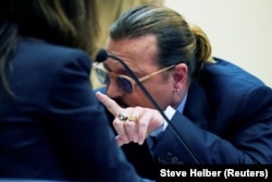 Aktor Johnny Depp berbicara dengan pengacaranya selama kasus pencemaran nama baik terhadap mantan istrinya, aktor Amber Heard, di ruang sidang di Fairfax County Circuit Courthouse di Fairfax, AS, 23 Mei 2022. (Foto: Steve Helber via REUTERS)