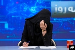 FILE - A TV anchor in a face covering bows her head while reading the news on TOLO News, in Kabul, May 22, 2022. The Taliban requires female TV anchors to cover their faces on-air.