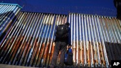 FILE - A migrant waits of the Mexican side of the border after United States Customs and Border Protection officers detained a couple of migrants crossing the U.S.-Mexico border on the beach, in Tijuana, Mexico, Jan. 26, 2022.
