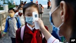 FILE - A teacher takes the body temperature of a schoolgirl to help curb the spread of the coronavirus before entering Kim Song Ju Primary School in Central District in Pyongyang, North Korea, Oct. 13, 2021.