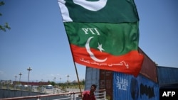 Seorang pendukung partai Pakistan Tehreek-e-Insaf (PTI), mengibarkan bendera di samping kontainer yang ditumpuk oleh pihak berwenang untuk memblokir Zona Merah menjelang aksi duduk yang direncanakan di Islamabad pada 24 Mei 2022. ( Aamir QURESHI / AFP)