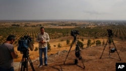 FILE - TV reporters work on a hilltop on the Turkey-Syria border overlooking Ras al-Ayn in northeastern Syria, Oct. 20, 2019. Journalists in northeastern Syria now face a requirement to join an official union before being credentialed.