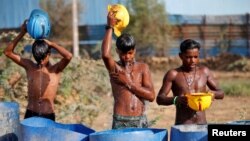 FILE - Workers use their helmets to pour water to cool themselves off near a construction site on a hot summer day on the outskirts of Ahmedabad, India, April 30, 2022. 