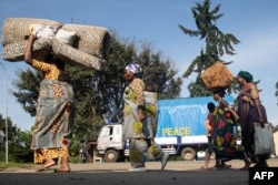 FILE - A group of Democratic Republic of Congo asylum-seekers carrying their belongings walk past a truck reading "PEACE" at the Bunagana border point in Uganda, on Nov. 10, 2021, during fighting between M23 rebels and DRC troops.