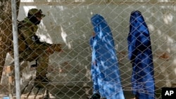 FILE - A Taliban fighter stands guard as two women enter the government passport office, in Kabul, Afghanistan, April 27, 2022. Afghanistan's Taliban leadership has ordered all Afghan women to wear the all-covering burqa in public.