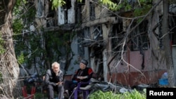 Local residents sit in a courtyard near a block of flats heavily damaged during the Ukraine-Russia conflict, in the southern port city of Mariupol, Ukraine, May 20, 2022. 