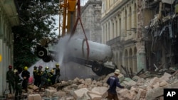 Firefighters spray a tanker truck with water to cool it down as they remove it from the site of a deadly explosion that destroyed the five-star Hotel Saratoga, in Havana, May 6, 2022.