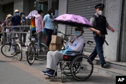 An elderly resident in a wheelchair waits under an umbrella as other elderly residents line up outside a bank to collect their pension as banking services reopen after pandemic measure lockdown are lifted, Tuesday, May 31, 2022, in Beijing. (AP Photo/Ng Han Guan)
