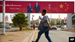 ແຟ້ມຮູບ-ແມ່ຍິງຄົນນຶ່ງກໍາລັງຍ່າງຂ້າມຖະໜົນ ໃກ້ກັບປ້າຍໂຄສະນາເພື່ອລະລຶກເຖິງການມາຢ້ຽມຢາມຂອງ ປະທານປະເທດຈີນ ທ່ານ ສີ ຈິ້ນຜິງ ໃນນະຄອນຫຼວງ ປອດມໍເຣສບີ, ປະເທດປາປົວນິວກີນີ, ວັນທີ 15 ພະຈິກ 2018.