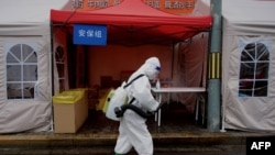 FILE - A worker wearing personal protective equipment disinfects the entrance to a residential area on lockdown due to the recent COVID-19 outbreaks in Beijing.