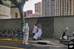 A worker in protective gear watches a barber cut a resident's hair Tuesday, May 31, 2022, in Shanghai, China. (AP Photo/Chen Si)