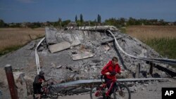 Teenagers on bicycles pass a bridge destroyed by shelling near Orihiv, Ukraine, May 5, 2022.
