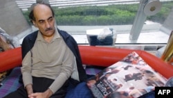 FILE - Mehran Karimi Nasseri looks at a poster of the movie inspired by his life, in the terminal 1 of Paris Charles De Gaulle airport, Aug. 12, 2004. Nasseri died Saturday in the airport at age 77.