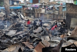 People inspect the damage as they stand amid the remains of properties that were burned by rioters in Kawangware slums in Nairobi, Kenya, Oct. 28, 2017.