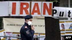 Petugas polisi berpatroli di depan spanduk yang dipasang oleh anggota Dewan Nasional Perlawanan Iran, sebuah kelompok oposisi Iran, di depan 'Grand Hotel Wien' selama pembicaraan nuklir tertutup dengan Iran di Wina pada 27 April 2021 (Foto: AFP)
