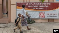 Une femme passe avec un enfant devant une banderole de parti politique au Bénin.