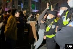 This frame grab from eyewitness video footage made available via AFPTV on November 27, 2022 shows demonstrators shouting slogans as police hold their positions, in Shanghai