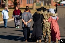 FILE - A female member of the military puts her arms around two female Afghan refugees at an Afghan refugee camp on Joint Base McGuire Dix Lakehurst, New Jersey, Sept. 27, 2021.