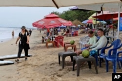 Turis tengah menikmati suasana pantai di Bali, Sabtu, 12 November 2022. Perekonomian Bali sedang membaik tetapi hanya menarik sepertiga dari wisatawan yang biasanya datang sebelum pandemi. (AP/Firdia Lisnawati)