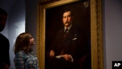FILE - A Museum of London employee poses for photographers next to an 1897 oil on canvas portrait of Sherlock Holmes at the Museum of London in London, Oct. 16, 2014. (AP Photo/Matt Dunham, File)