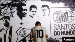 Seseorang berdiri di depan gambar legenda sepak bola Brazil Pele saat orang-orang berkumpul untuk berduka atas kematiannya, di Santos, Brazil, 29 Desember 2022. (Foto: Reuters)