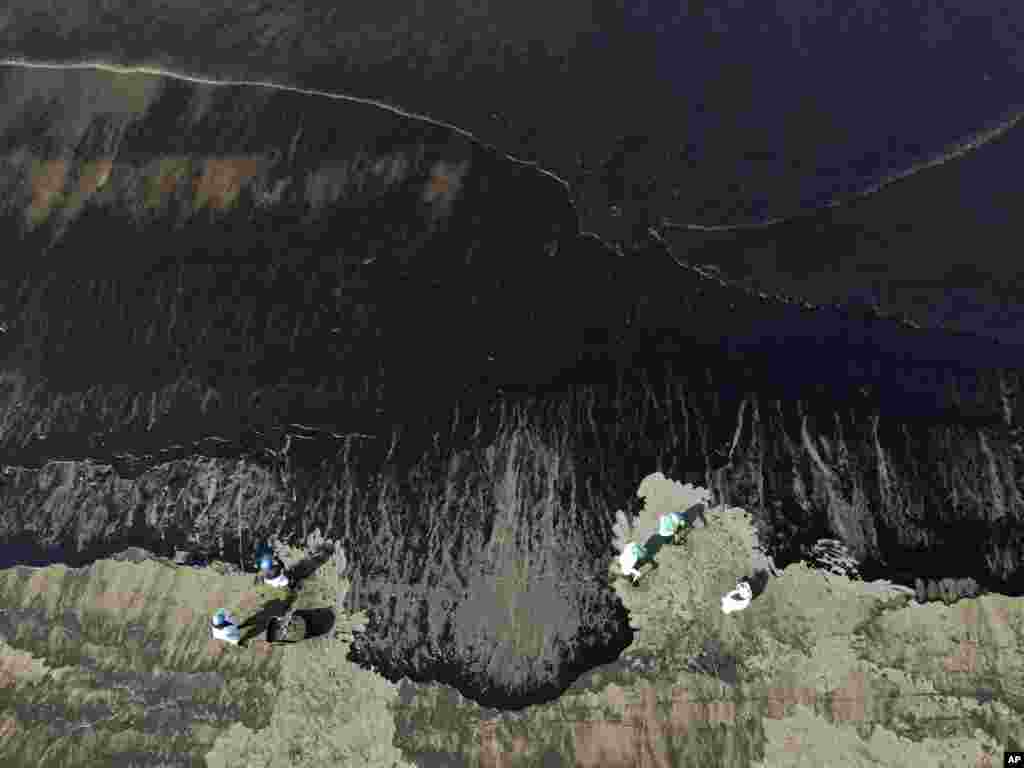 Workers clean oil from Cavero beach in Ventanilla, Callao, Peru, Jan. 18, 2022. The Peruvian Civil Defense Institute said the eruption of an undersea volcano in Tonga created high waves that moved a ship loading oil into La Pampilla refinery, causing the oil to spill.