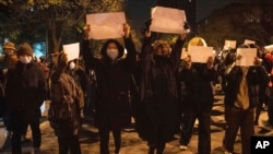FILE - Protesters hold up blank papers and chant slogans as they march in protest in Beijing, Nov. 27, 2022.