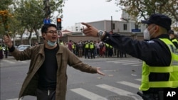 A protester holding flowers is confronted by a policeman during a protest on a street in Shanghai, China, Nov. 27, 2022. Authorities eased anti-virus rules in scattered areas but affirmed China's severe "zero-COVID" strategy Monday.