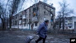 A local woman walks to the distribution point of humanitarian aid in front of housing which was damaged by Russian shelling in Kupiansk, Kharkiv region, Ukraine, Dec. 28, 2022. 