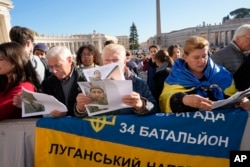 Lyudmilla Panasyuk (kanan), bersama ibunya Maryia Luzakova (tengah), memajang foto putranya Yuki Panasyuk, dan foto tentara lain dari batalion ke-34 brigade ke-57 Angkatan Darat Ukraina, yang mereka klaim telah menghilang di jalan Luhansk di Ukraina saat menghadiri audiensi umum mingguan Paus Fransiskus di Lapangan Santo Petrus di Vatikan, Rabu, 23 November 2022. (AP/Andrew Medichini)